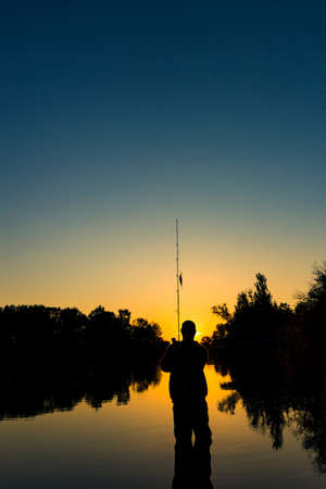 Fishing on the lake at sunset. Silhouette of a fishermanの写真素材
