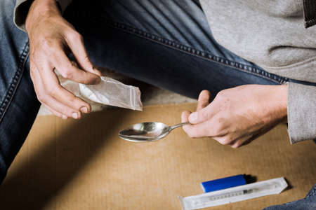 A young man makes heroin in, preparing to take heroin, pours heroin into a spoon. The concept of crime and drug addiction.の写真素材