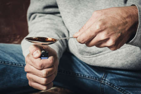 The hands of a drug addict melting cocaine in a spoon. A man holds a spoon over a cigarette lighter. Drugs and the concept of crime.の写真素材