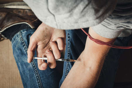Addict man with a syringe in action. The concept of drug abuse and traffic.の写真素材
