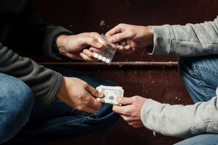Hand of addict man with money buying dose of cocaine or heroine or another narcotic from drug dealer. Drug abuse and traffic concept.の写真素材
