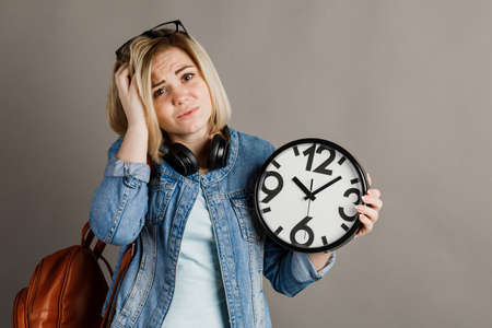 Girl student with a big clock in hands. on a gray background.
