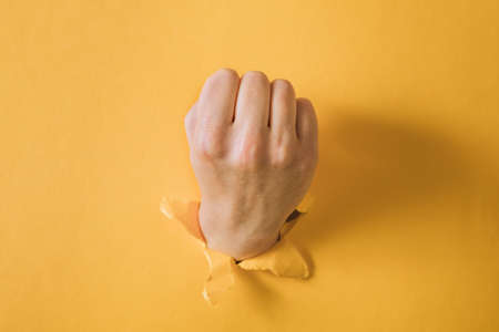 female fist punching through a paper, isolated on a yellow backgroundの写真素材