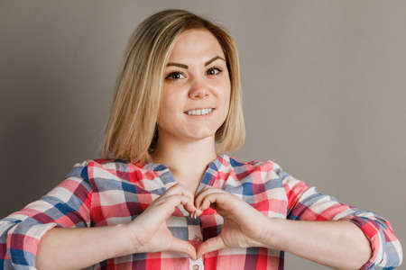 A girl shows the heart sign of a hand on a gray background