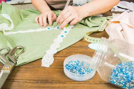 A woman is making jewelry, a home workshop. Female hands that create an accessory with beads and...