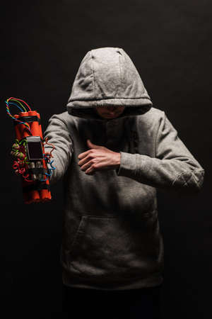 The silhouette of a man in the hood on a black background, his face is not visible, shows hands gesture and a time bomb. The concept of criminal terrorismの写真素材