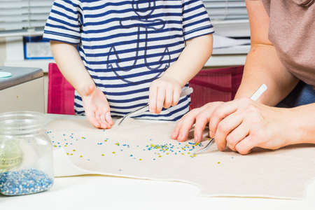 Mother and child make a pattern of beads on the fabric. Workplace for handicraft creativity.の写真素材