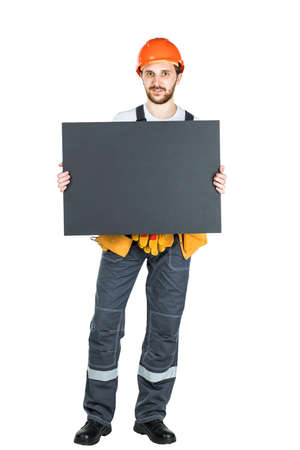 Full length portrait of a male construction worker with a white blank banner over a white wall background. repair and construction. Isolated over white backgroundの写真素材