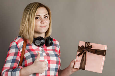 Portrait of a young woman holding a gift. Student in checkered shirt on gray background.