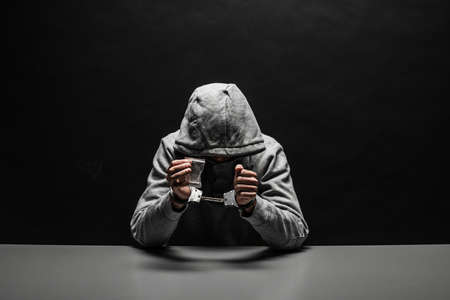 The drug addict was arrested for drug use at the table. suffering from addiction on a dark black backgroundの写真素材