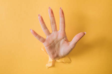 girl hand breaks the yellow paper and shows a gesture.の写真素材