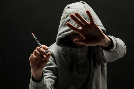 Addict in gray hoodie on the head suffers from addiction on a dark black background.