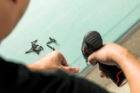 Builder spins the screw into a sheet of drywall. Construction and repair concept.