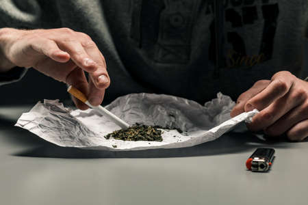 A drug addict makes a cigarette with marijuana. The concept of drug abuse and trafficの写真素材