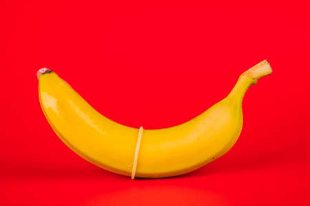 Condom and banana on a red background close-up.の写真素材