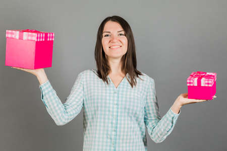 Portrait of cheerful beautiful girl with shining smile holding two gifts on her hands looking at camera isolated on grey background, advertising conceptの写真素材