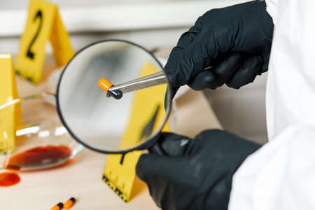 A policeman looks through a magnifying glass at the evidence at the crime scene. The crime scene of poisoning and overdosing.の写真素材