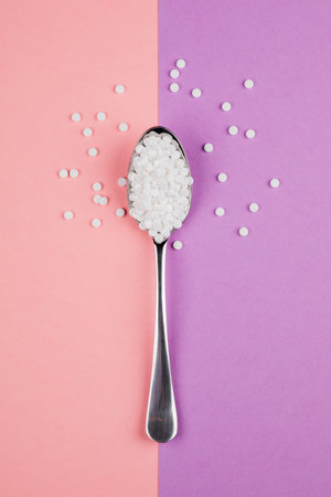 Sugar-replacing tablets with a spoon on a pink and purple background.