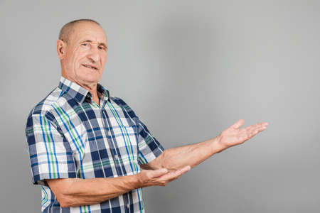 The elderly person point away. Serious Mature man pointing finger to the side, on grey background, copy space.の写真素材