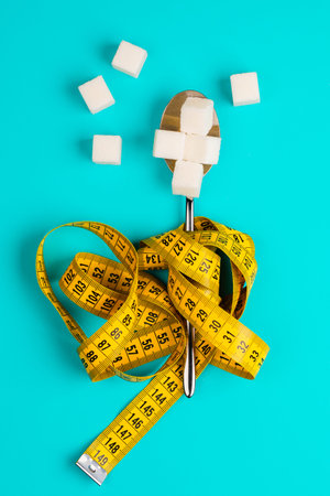 Sugar-replacing tablets or sugar with a spoon are entangled in the measuring tape. On a blue...