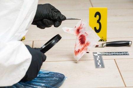 A criminology expert looks through a magnifying glass at a bloody napkin at the crime scene.