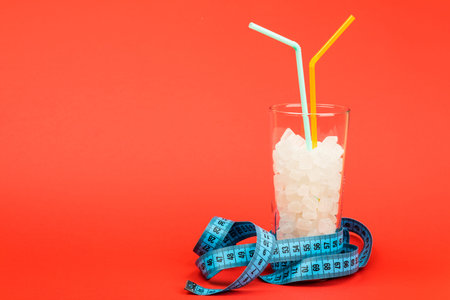 A glass of sugar cubes is a concept of unhealthy food. On red background.
