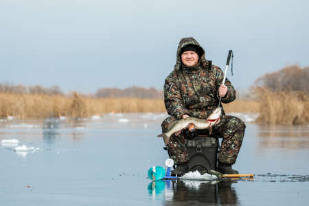 A young man is fishing from a hole on ice. Winter fishing.の写真素材