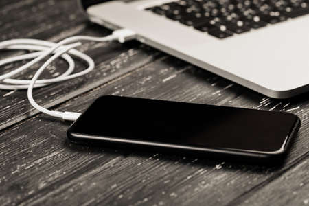 A USB cable connects your phone and laptop. On the black table