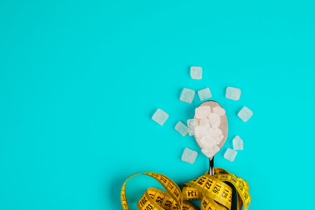 Sugar-replacing tablets or sugar with a spoon are entangled in the measuring tape. On a blue...