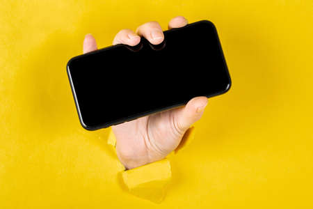 A woman holding a phone through a torn yellow paperの写真素材