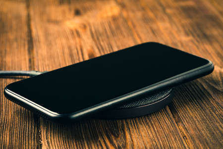 Charge your smartphone on the charging pad. Wireless charging on wooden table. rendered imageの写真素材
