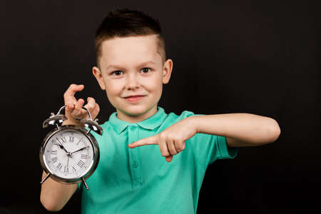 Boy holding an alarm clock. Baby isolated on black background. Concept of time. The child, pointing...