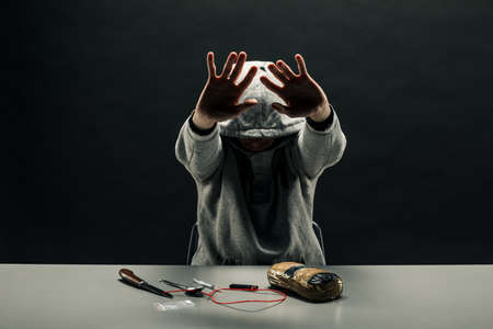 A man sitting at a table with drugs, hides his face Concept: a criminal with drugsの写真素材