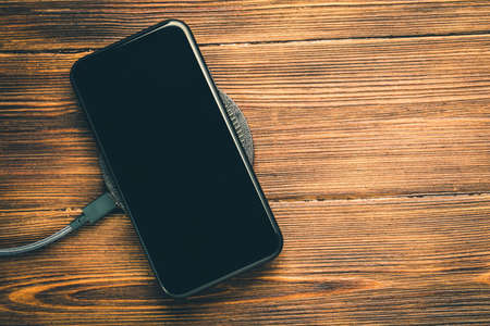 Charge your smartphone on the charging pad. Wireless charging on wooden table. rendered imageの写真素材