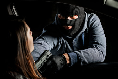 A masked robber with a gun threatens a woman in a car. robbery.