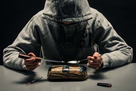 man is a drug addict sitting at the table makes drugs. The concept of social problems of drug...
