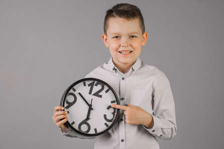 boy wearing a plaid shirt and holding a watch, on a gray wall background, children portrait Studio. People sincere emotions, the concept of children's lifestyle. Copy space layout.の写真素材