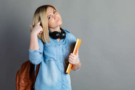 portrait of a beautiful girl student with a backpack and textbook the book in the hands of smiling on gray background. attractive, positive girl high school studentの写真素材