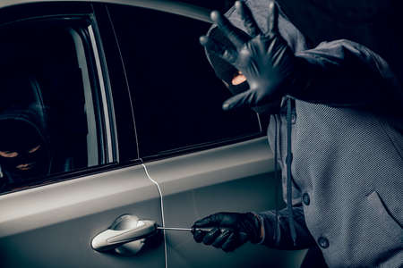 A man with a Balaclava on his head tried to break into the car. He uses a screwdriver. Hijacker, the concept of car theftの写真素材