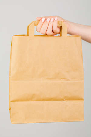 Close-up of woman holding brown empty paper bag isolated on white background. The concept of service delivery.の写真素材