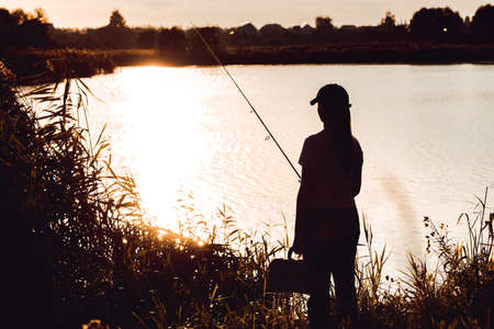 Silhouette of a woman at sunset with a fishing rod near the pondの写真素材