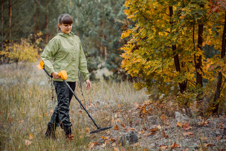 young girl looks at the monitor of a metal detector on the background of the forest.