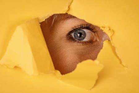 Young woman looking through torn yellow paperの写真素材