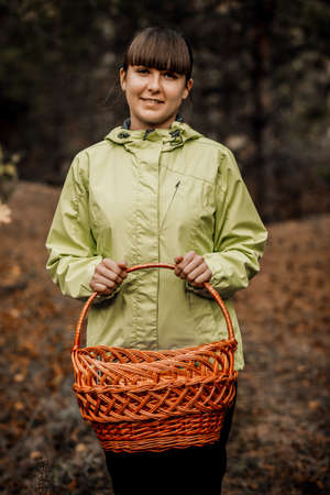 A woman with a basket collects mushrooms in the autumn forest.