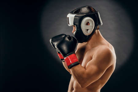 Portrait of a young man with a Boxing helmet and gloves on a dark backgroundの写真素材