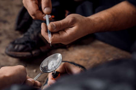 Two shabby  men preparing drug injection in slums.の写真素材