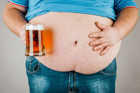 A man with a fat belly holding a glass of beer. On gray backgroundの写真素材