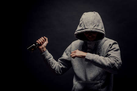 A dangerous hooded man stands in the dark and holds a broken bottle. The face is not visible. The concept of crime, murder.の写真素材