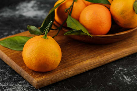 a plate with some tangerines and cutting board on marble background.