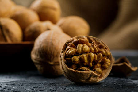 peeled walnut and plate with some raw walnuts on dark table.